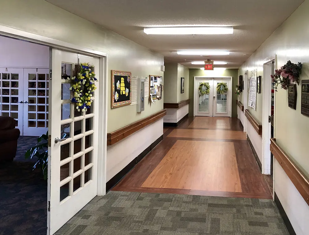 Well-lit hallway at Caremoor Assisted Living featuring seasonal wreaths, wall décor, and bulletin boards