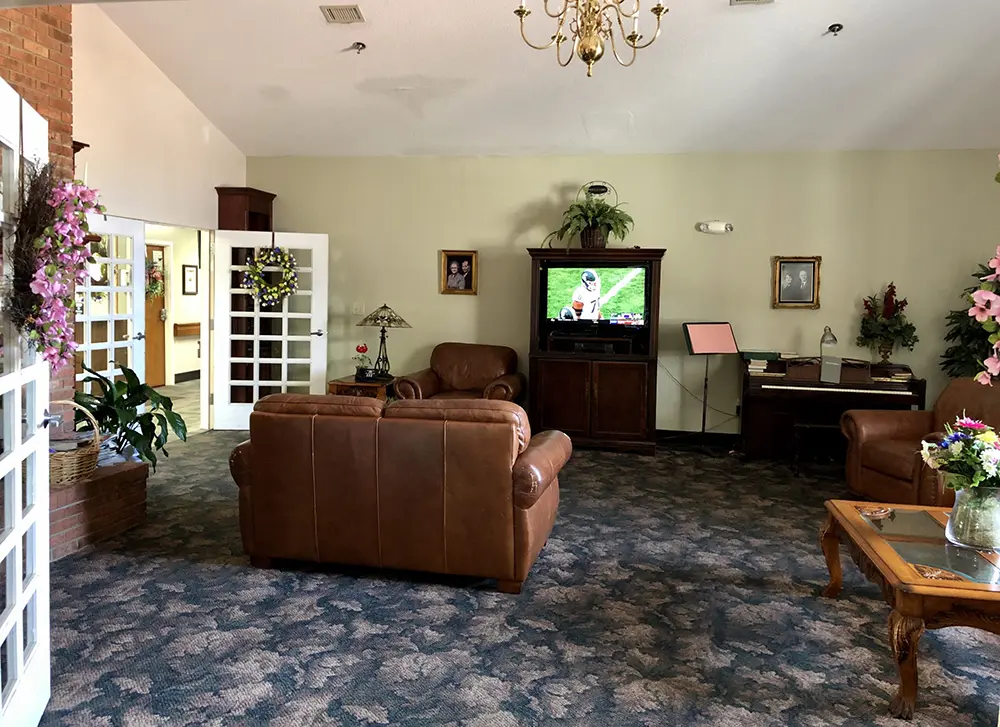 Spacious lounge at Caremoor Assisted Living with leather seating, floral décor, and a TV entertainment center