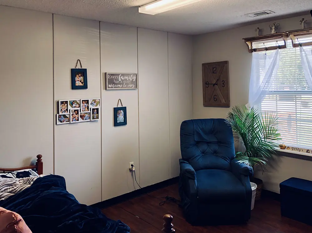Comfortable private room at Caremoor Assisted Living featuring a recliner, wall art, family photos, and natural light from a window
