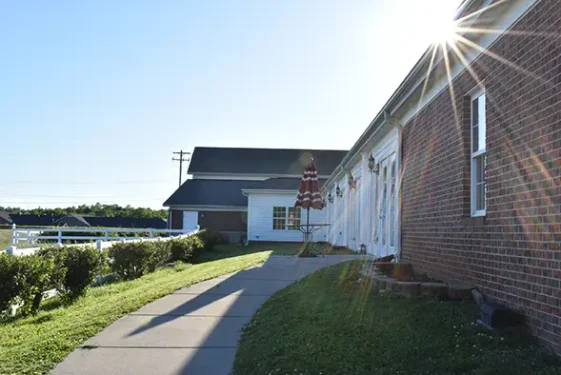 Pathway leading to LaMoor Commons with a sunflare effect, a red and white striped umbrella, and a brick building on a sunny day.